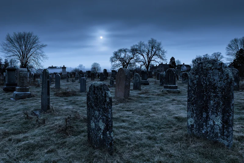 Old rural cemetery at night with rows of weathered stone tombstones under moonlight