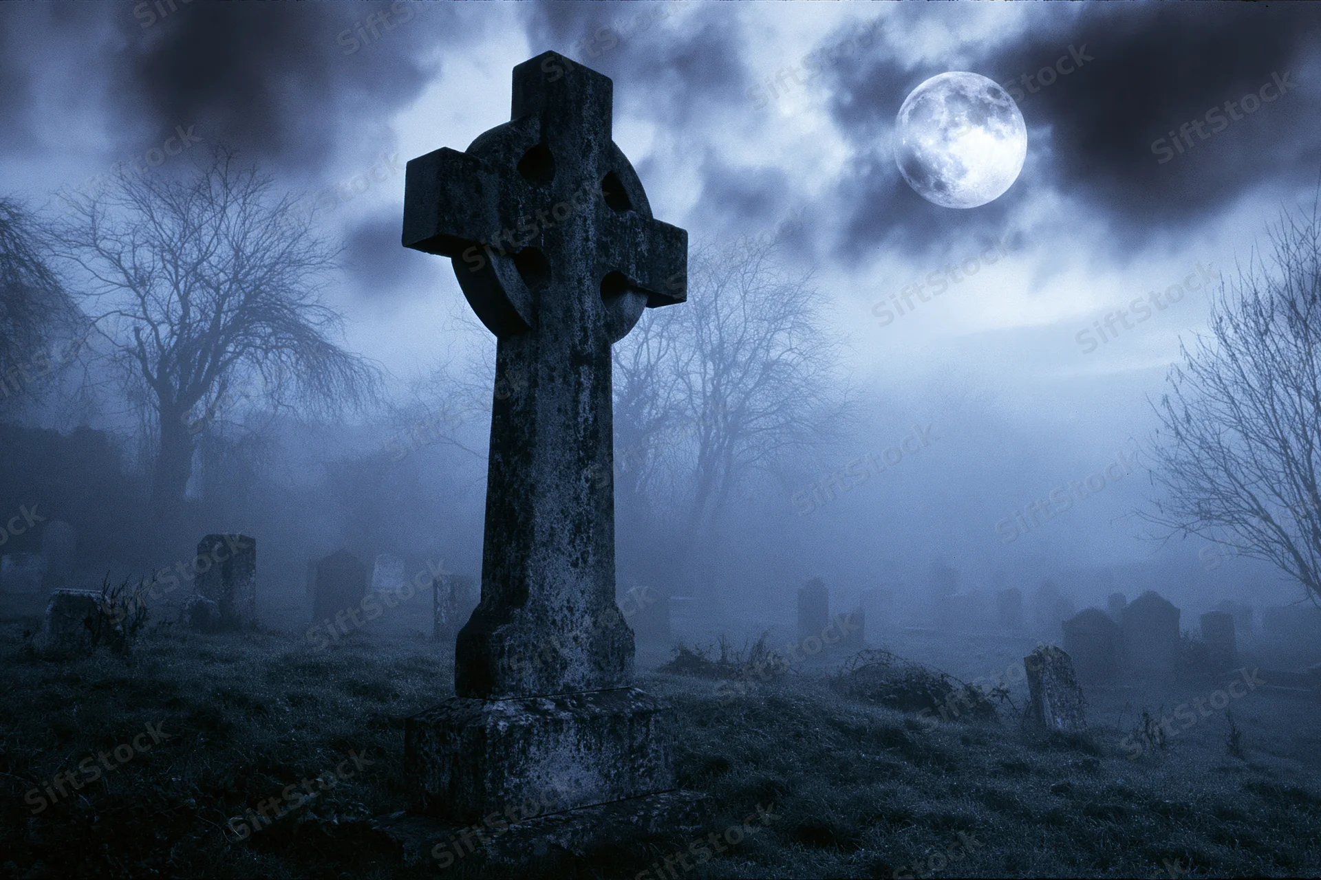 Old stone cross gravestone standing in a foggy cemetery at night under a full moon