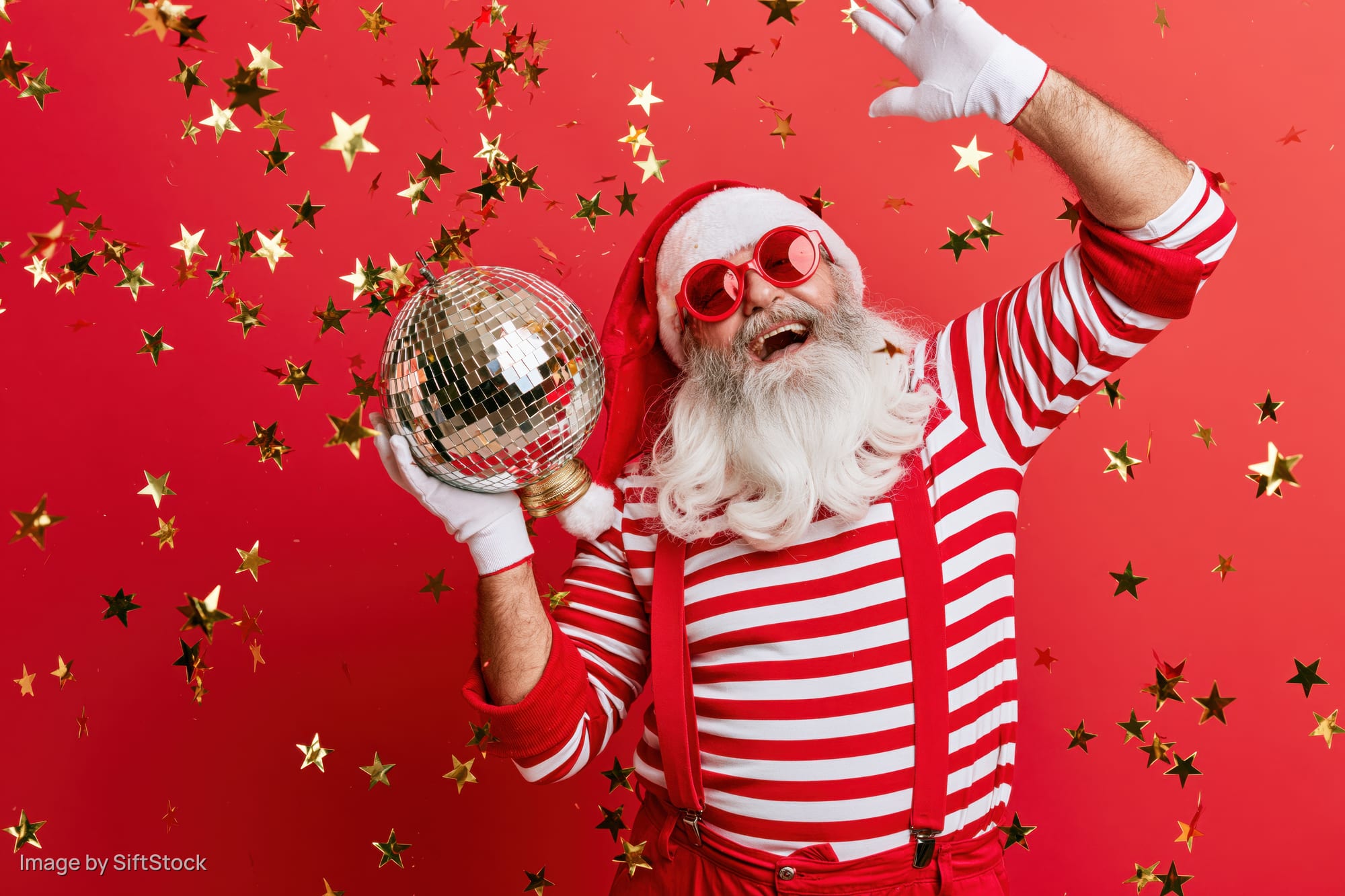 Older man dressed as santa claus in striped shirt and suspenders holding disco ball with confetti falling around him