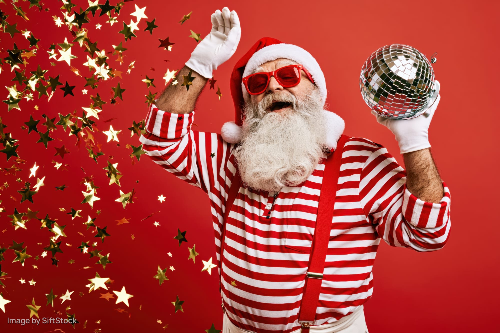 Older man dressed as santa claus in striped shirt and sunglasses dancing with disco ball and confetti against red background