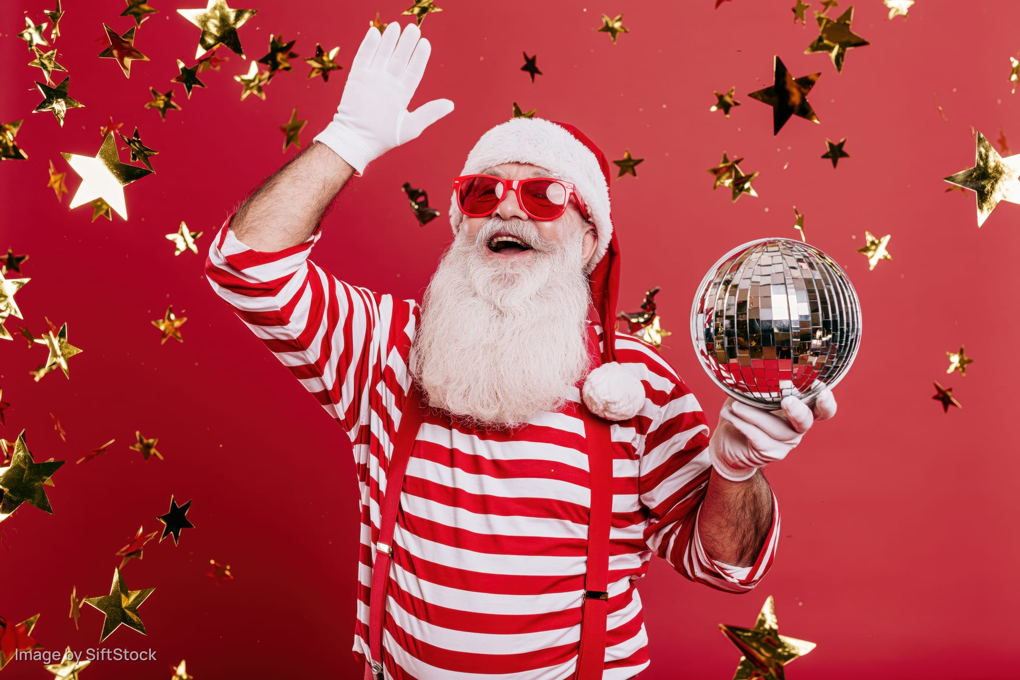 Man dressed as santa claus waving and holding a disco ball against a red background with falling stars