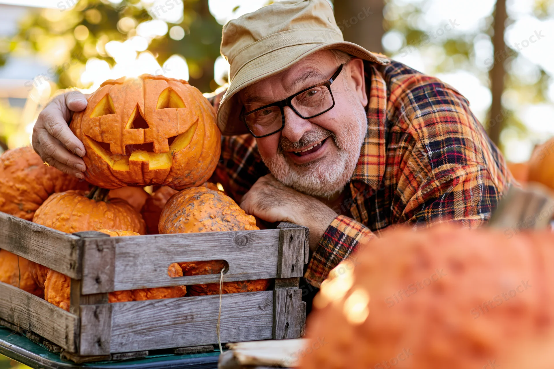 Senior man smiling beside a wooden crate of carved pumpkins in an outdoor garden setting
