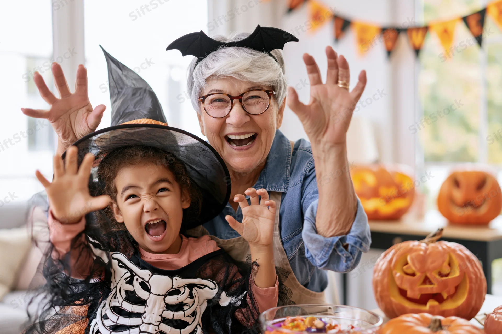 Grandmother and granddaughter in halloween costumes waving together at home