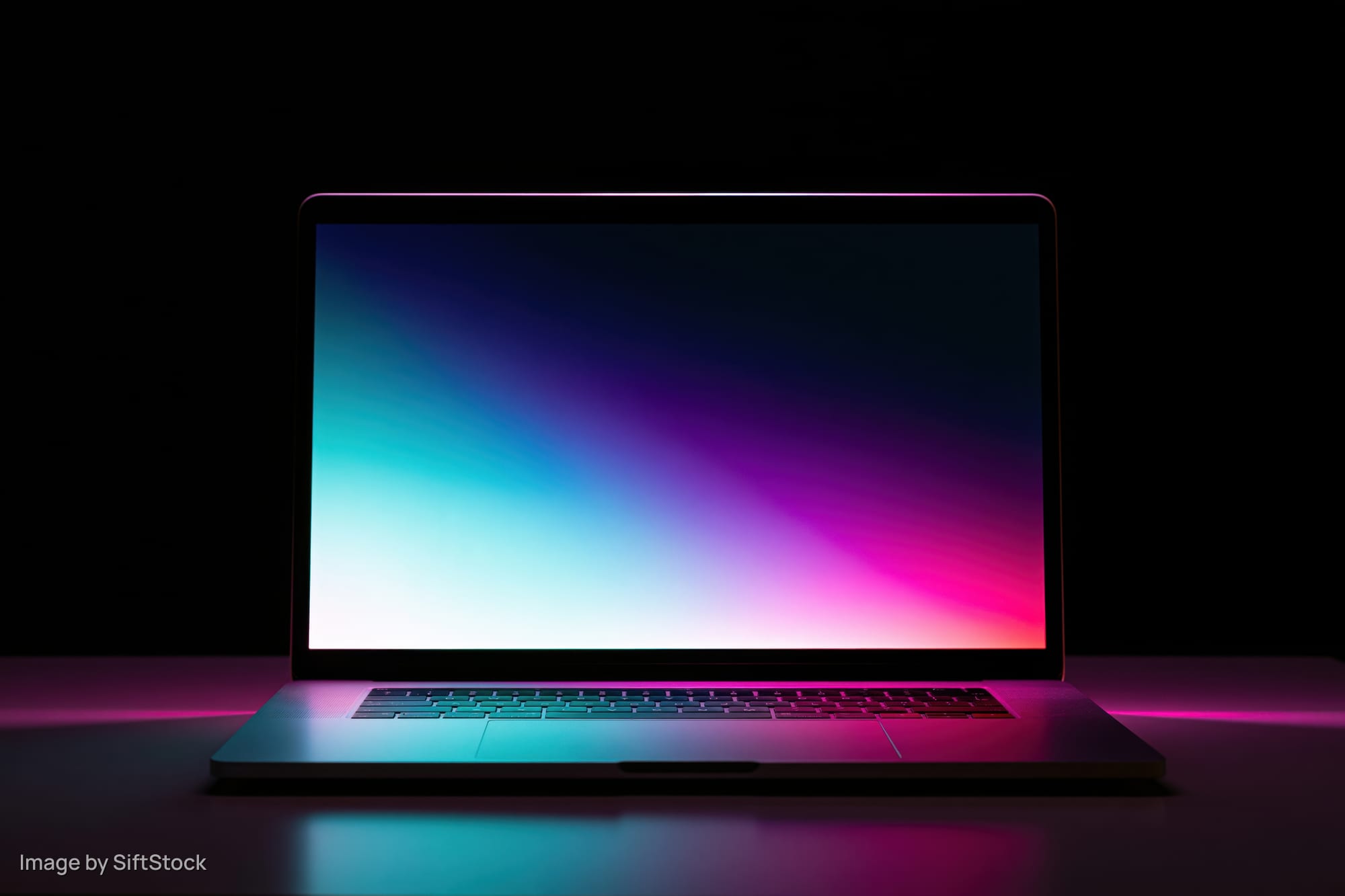Open aluminum laptop with glowing screen displaying colorful gradient in dark studio setting