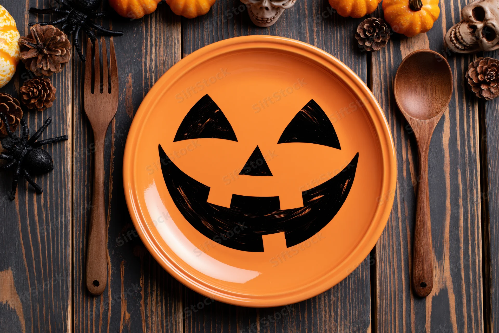 Orange ceramic plate with jack-o-lantern face on dark wooden table surrounded by halloween decorations