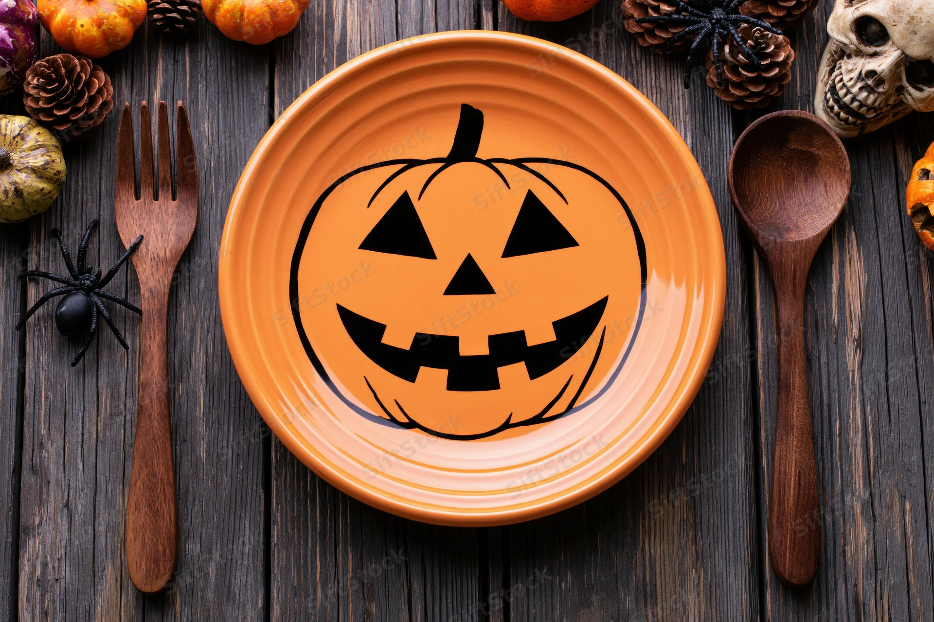 Orange ceramic plate with jack-o-lantern design on dark wooden table surrounded by halloween decorations
