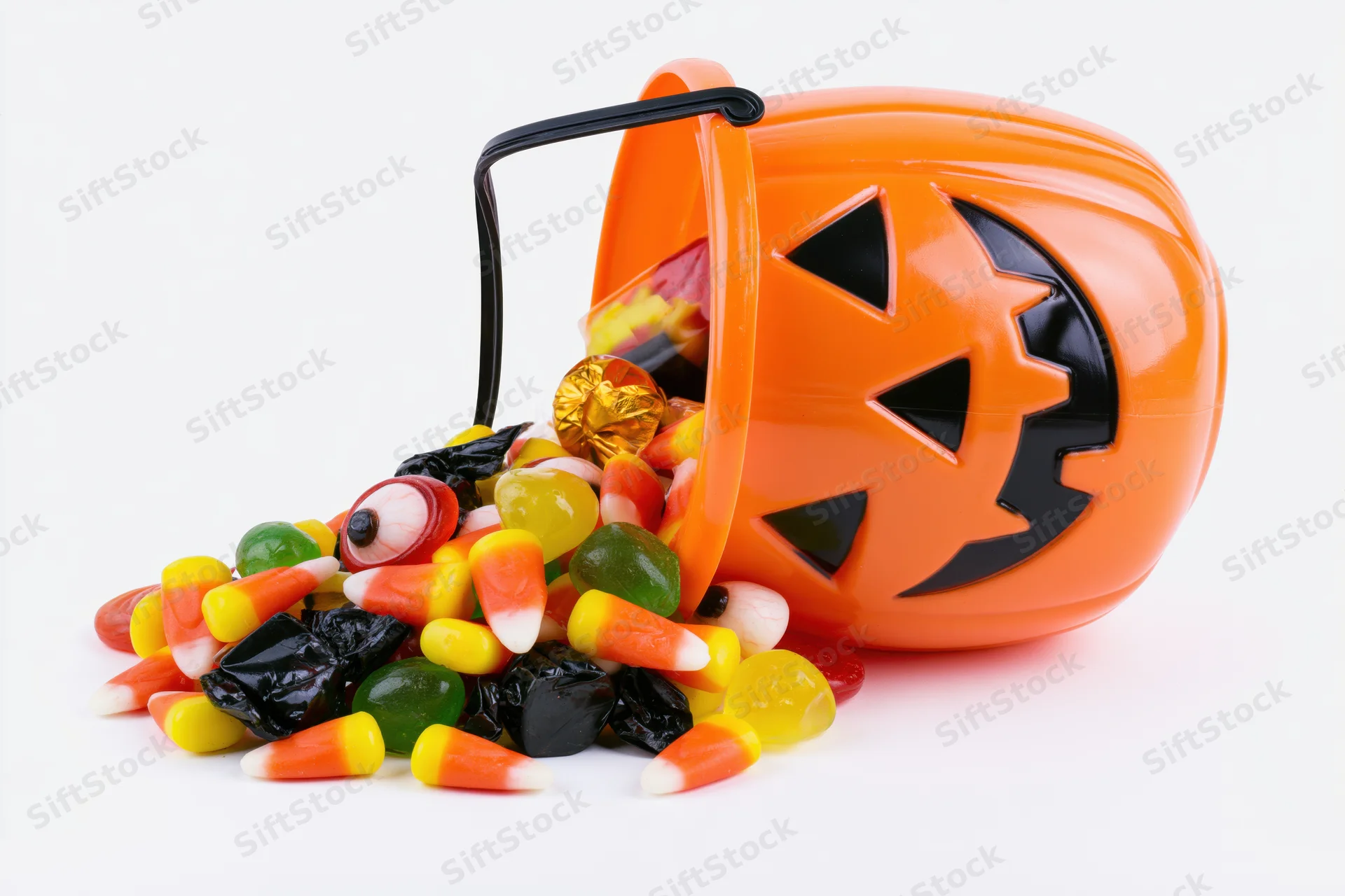 Orange plastic jack-o-lantern bucket tipped over spilling candy on white background