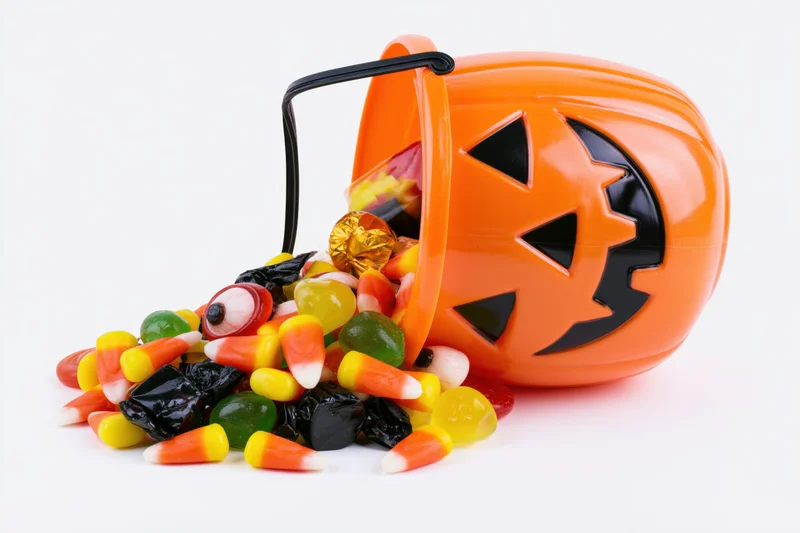 Orange plastic jack-o-lantern bucket tipped over spilling candy on white background