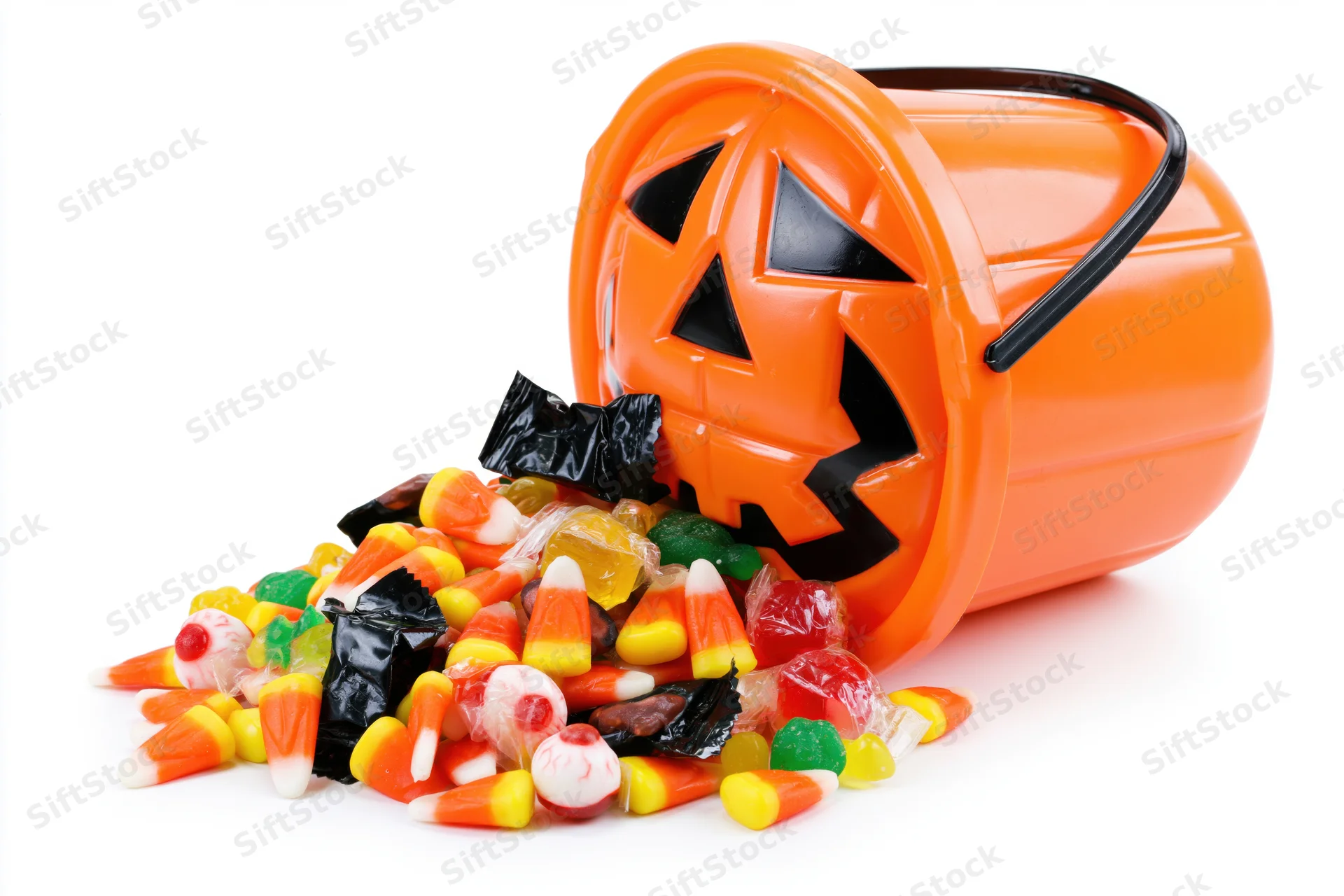 Orange plastic jack-o-lantern bucket tipped over with spilled candy on white background