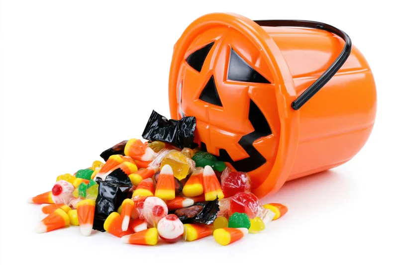 Orange plastic jack-o-lantern bucket tipped over with spilled candy on white background