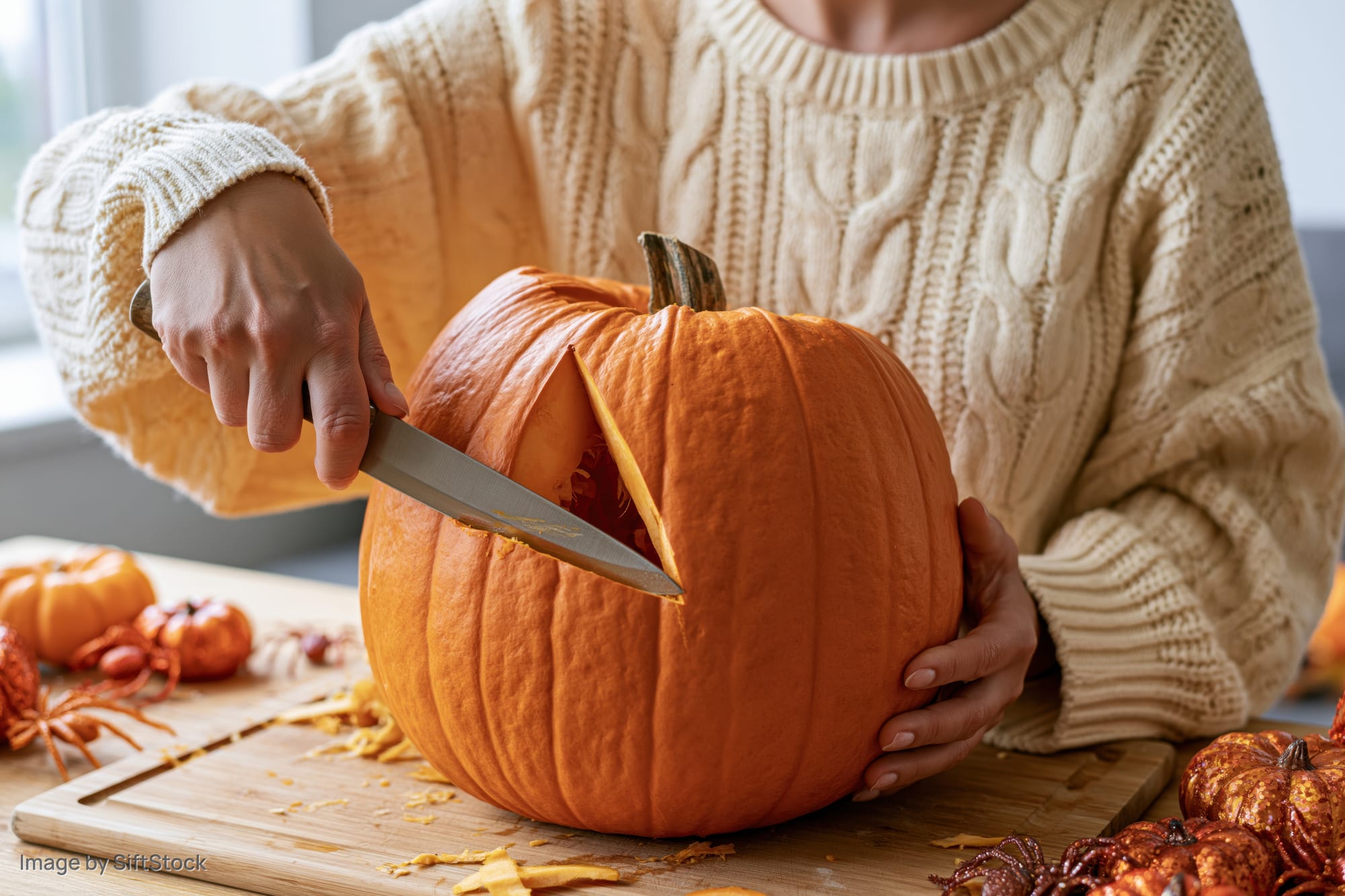 Woman carving a large orange pumpkin on a wooden cutting board in a kitchen