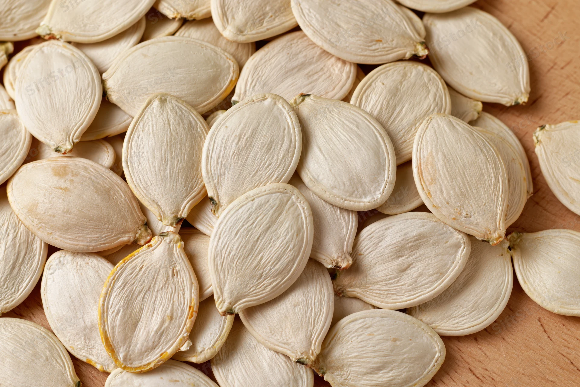Closeup of raw white pumpkin seeds piled on a wooden surface