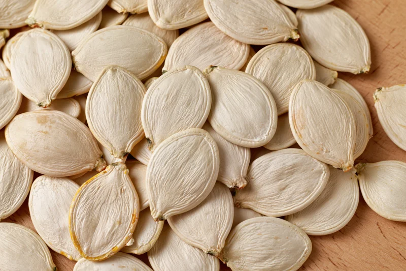 Closeup of raw white pumpkin seeds piled on a wooden surface