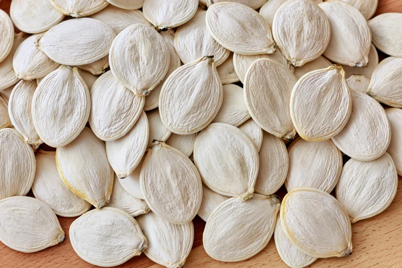 Closeup of raw white pumpkin seeds piled on a wooden surface