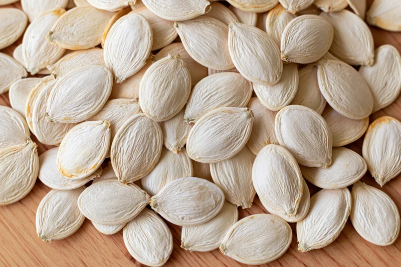 Pile of raw white pumpkin seeds on wooden surface filling frame