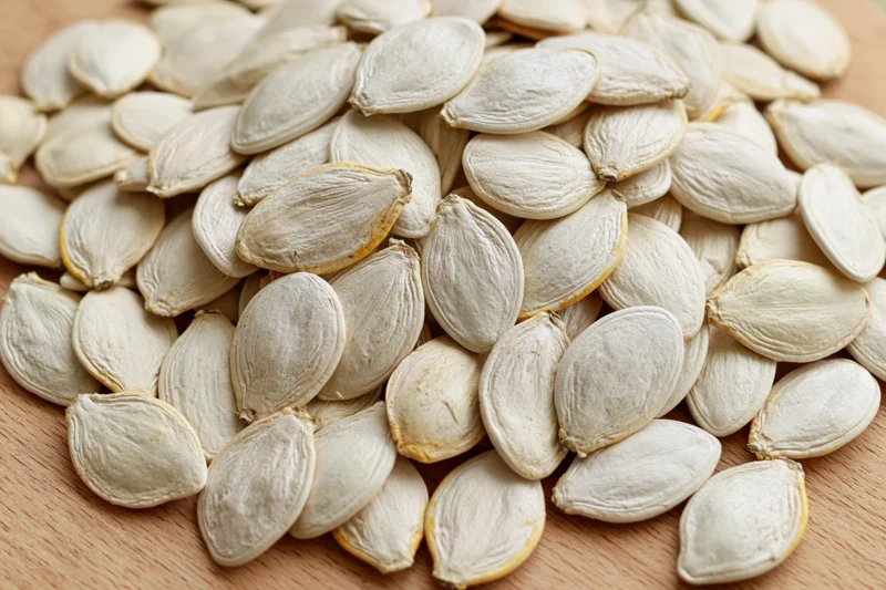 Pile of raw white pumpkin seeds on wooden surface