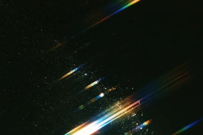 Rainbow light streaks and lens flare effects across a dark abstract background
