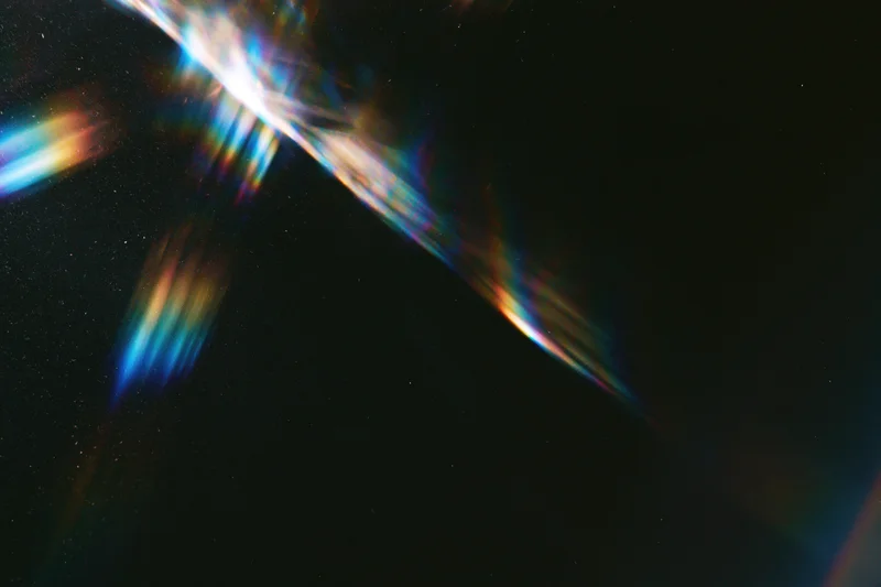 Rainbow light refraction and lens flare streaks across a dark background