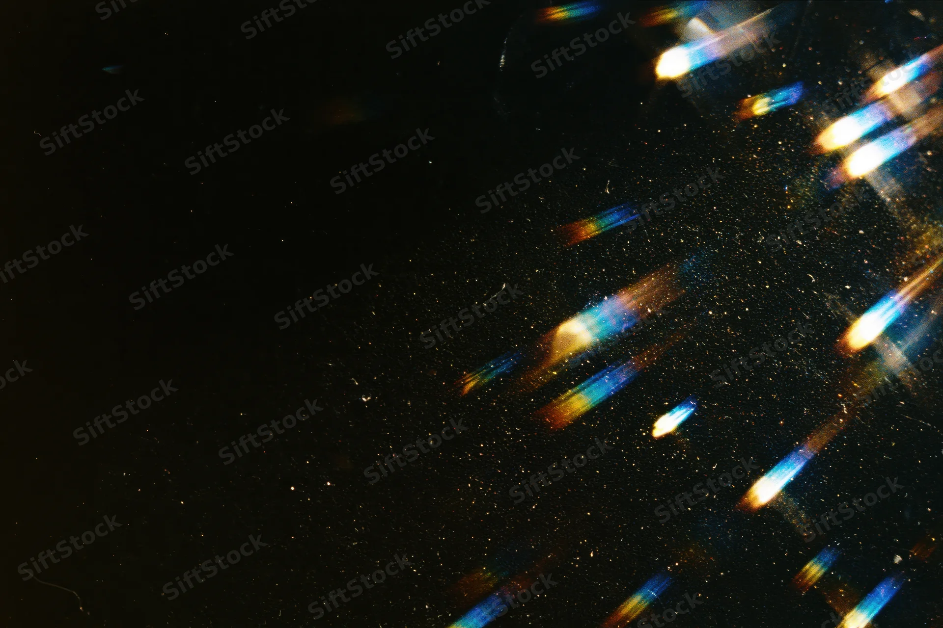 Rainbow light streaks and lens flare effects scattered across a dark background with sparkling particles