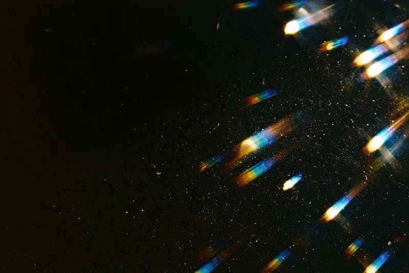 Rainbow light streaks and lens flare effects scattered across a dark background with sparkling particles
