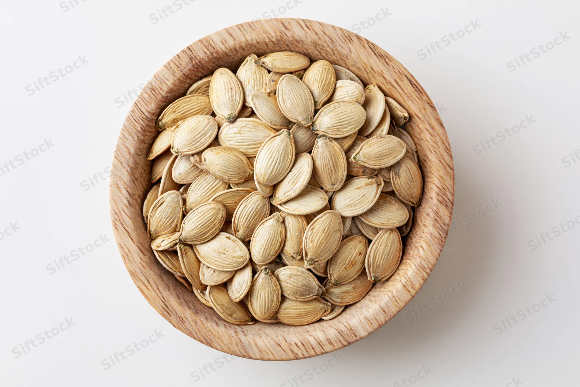 Raw pumpkin seeds filling a small round wooden bowl on white surface