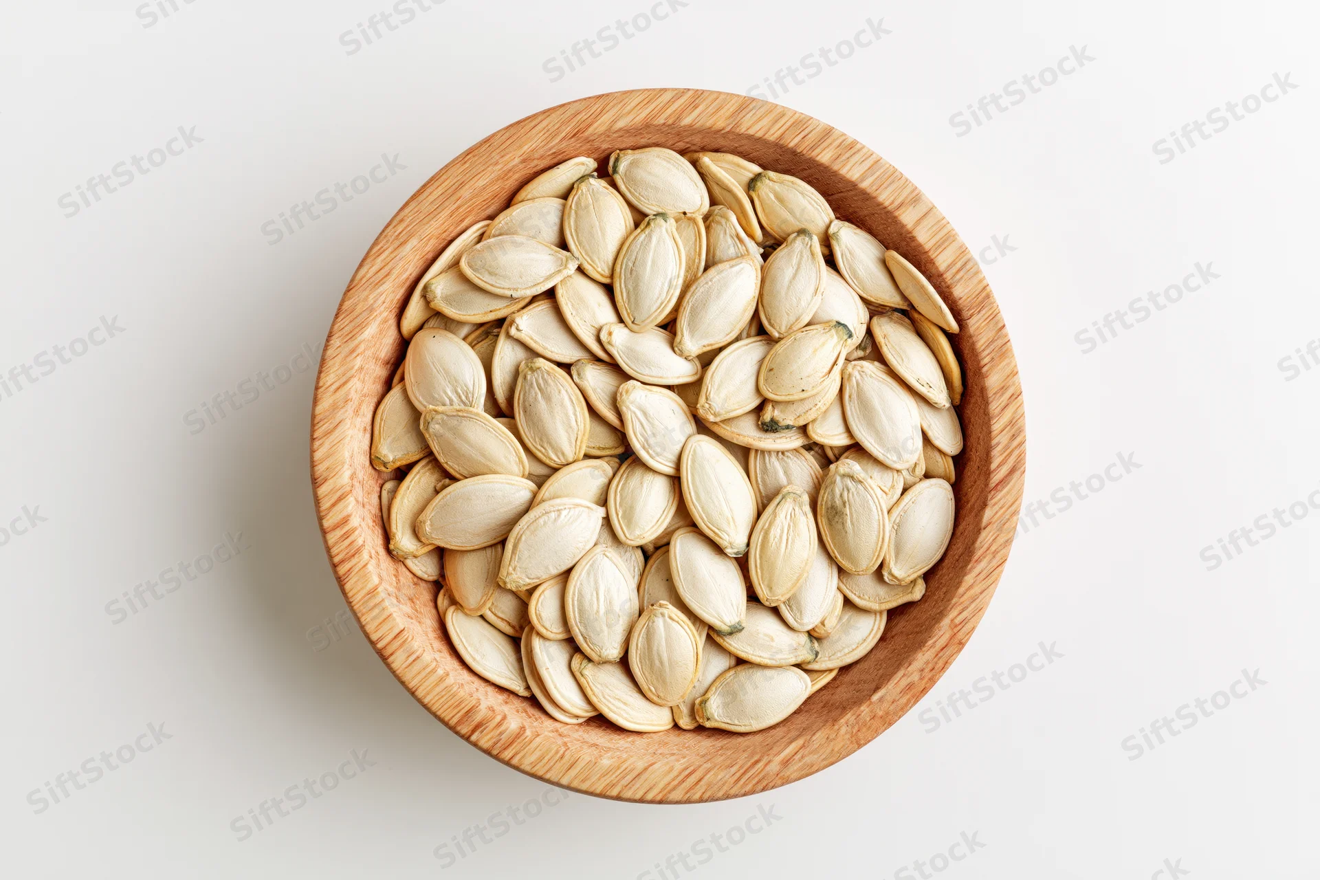 Raw pumpkin seeds in a round wooden bowl on white surface