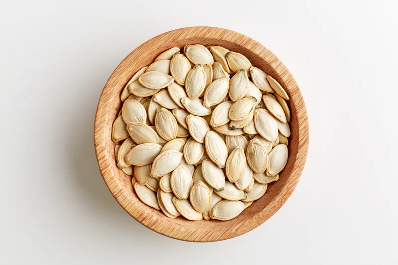 Raw pumpkin seeds in a round wooden bowl on white surface