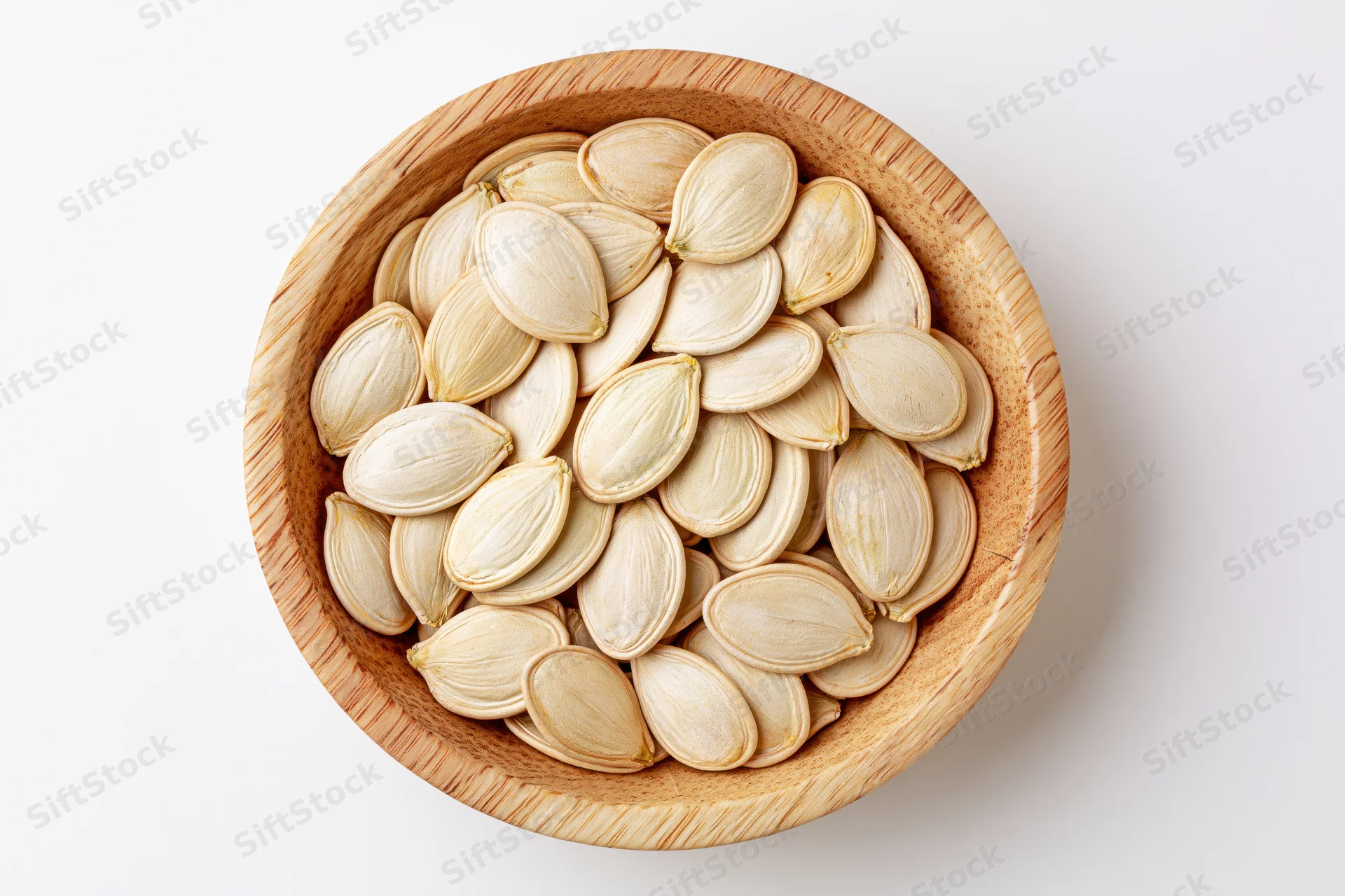 Raw pumpkin seeds filling a small round wooden bowl on white background