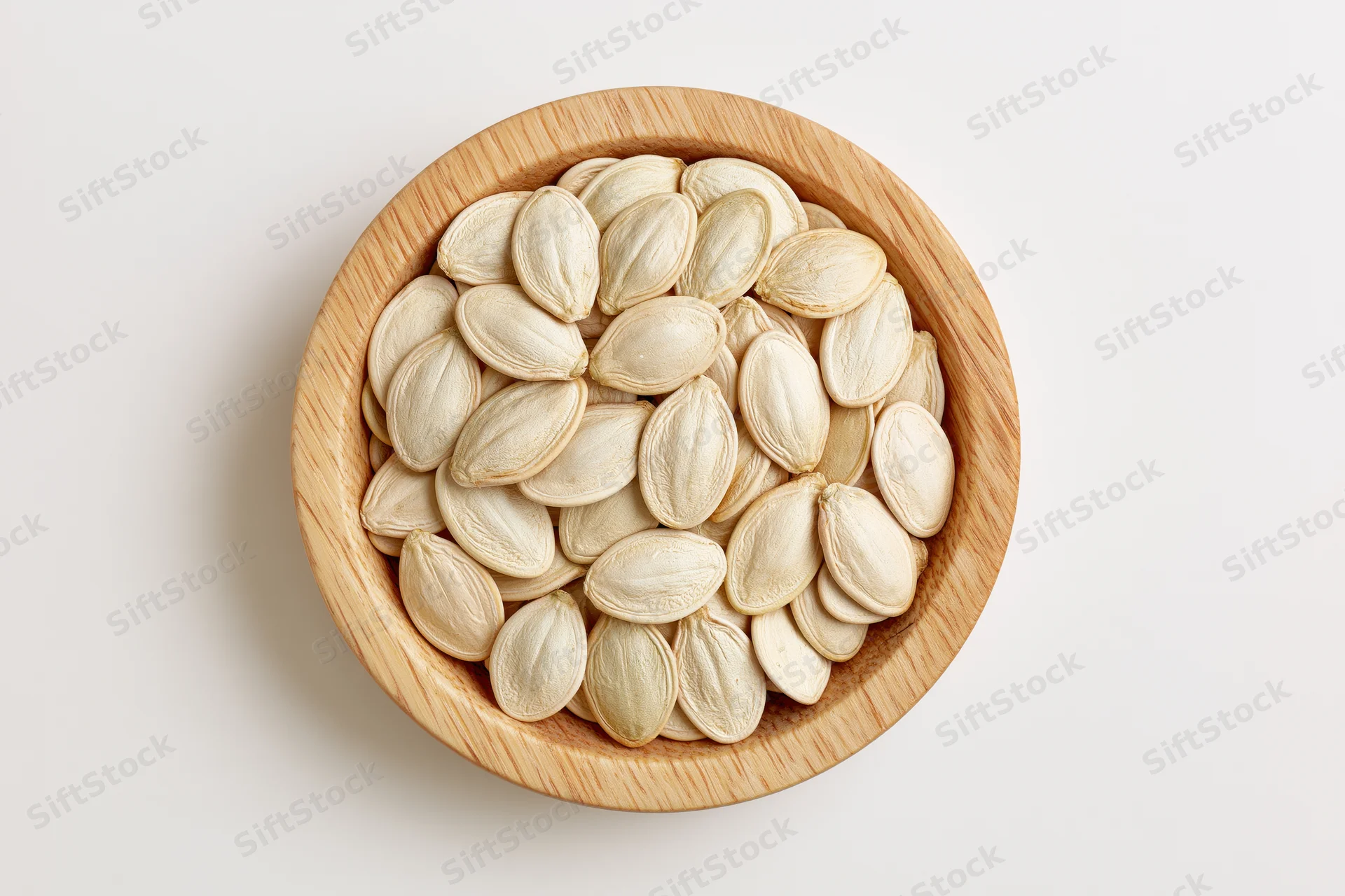 Raw pumpkin seeds filling a small round wooden bowl on a white surface