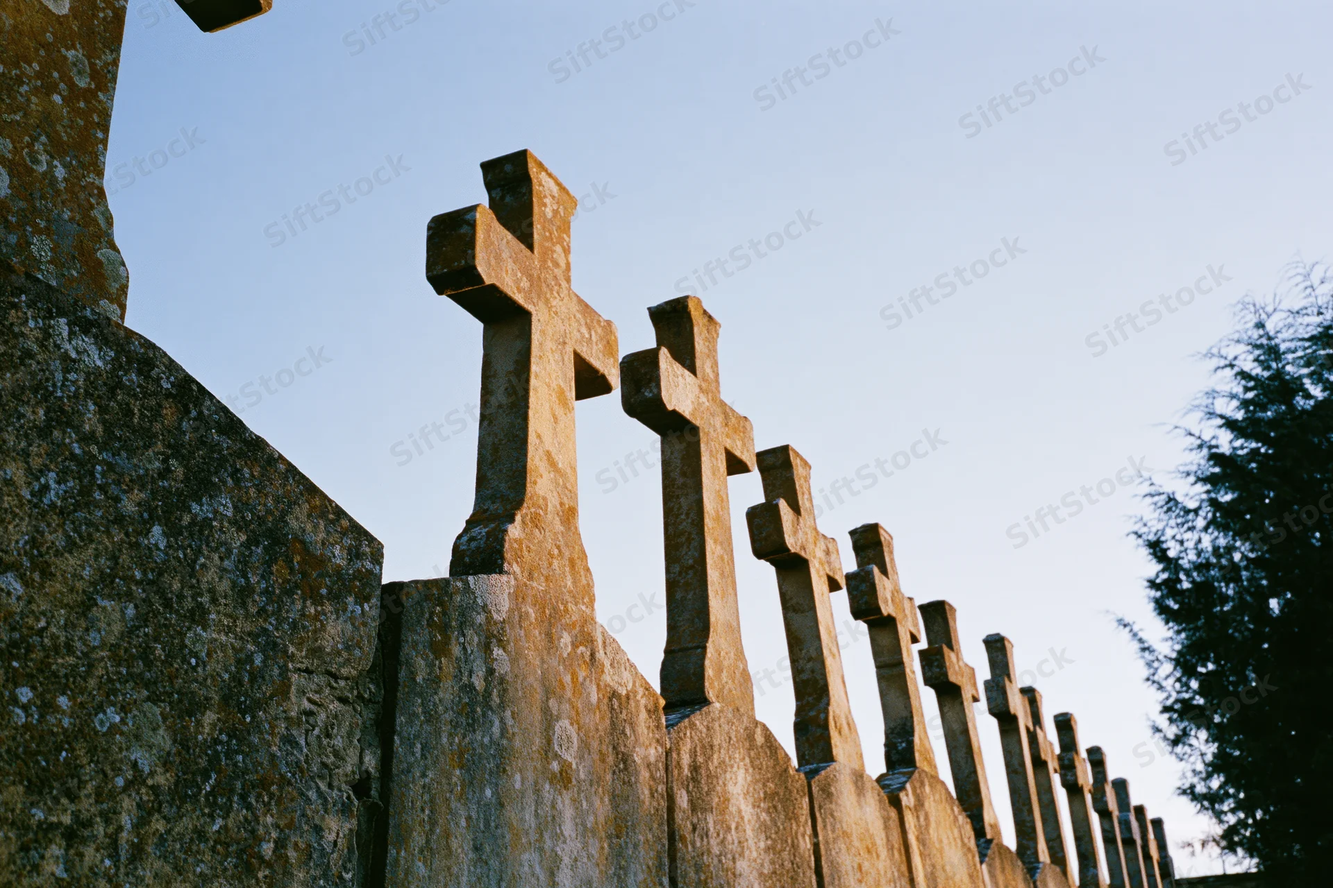 Row of weathered stone crosses on grave markers in a cemetery under twilight sky