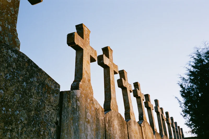 Row of weathered stone crosses on grave markers in a cemetery under twilight sky