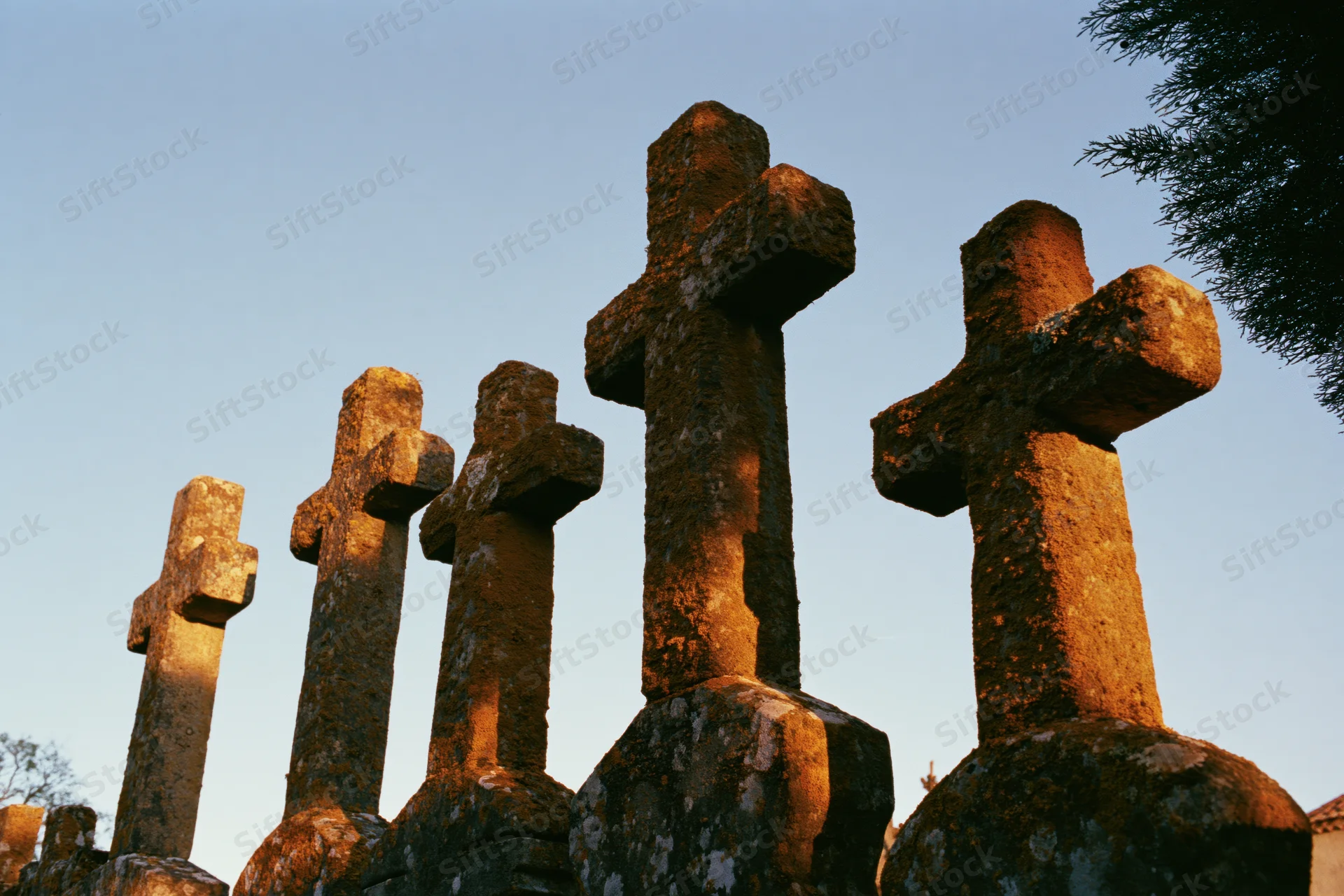 Row of weathered stone crosses in a cemetery at dusk