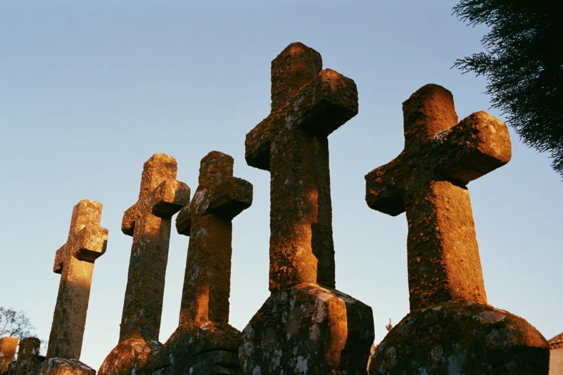 Row of weathered stone crosses in a cemetery at dusk