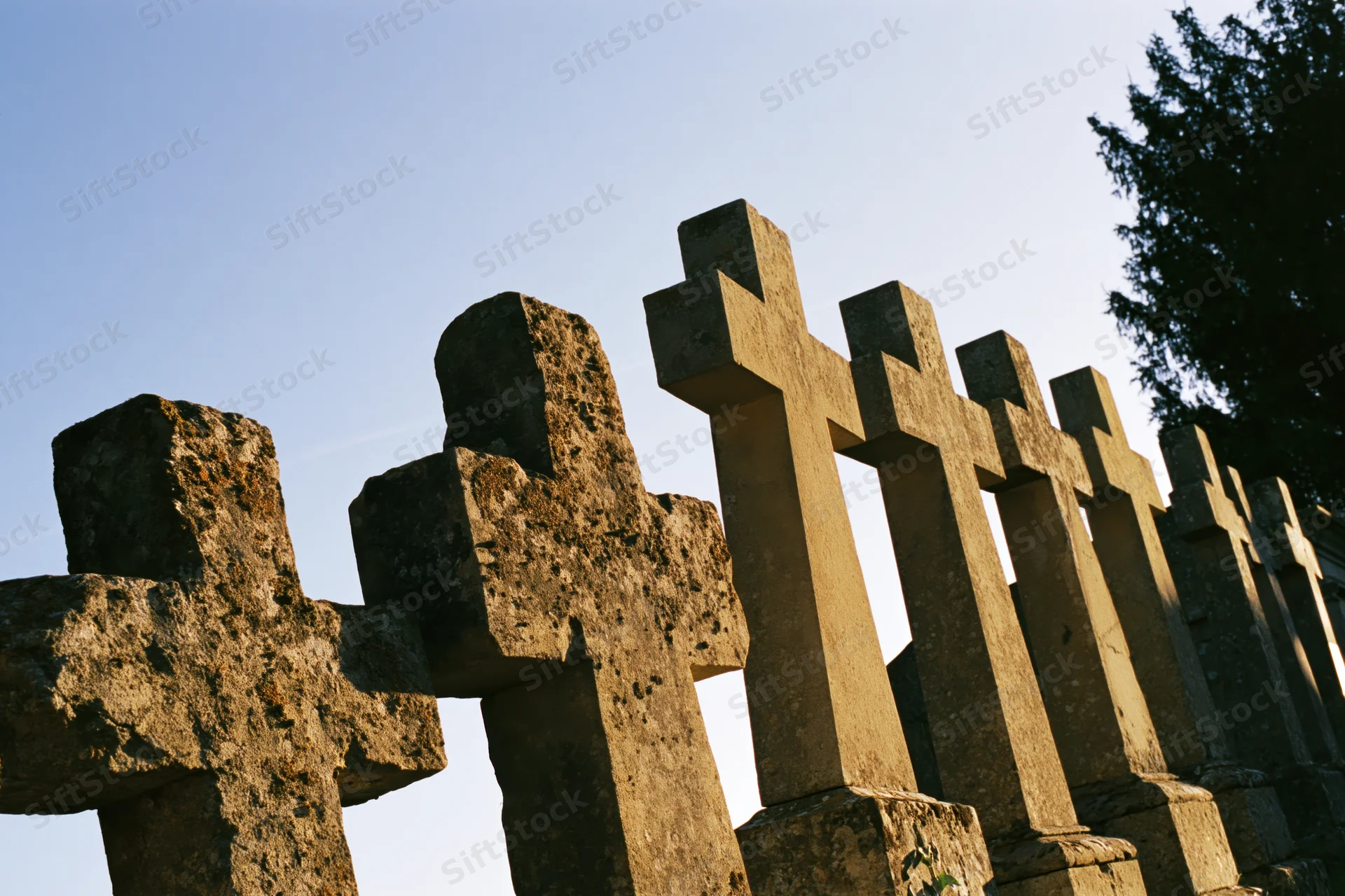 Row of weathered stone crosses standing in a cemetery under clear sky