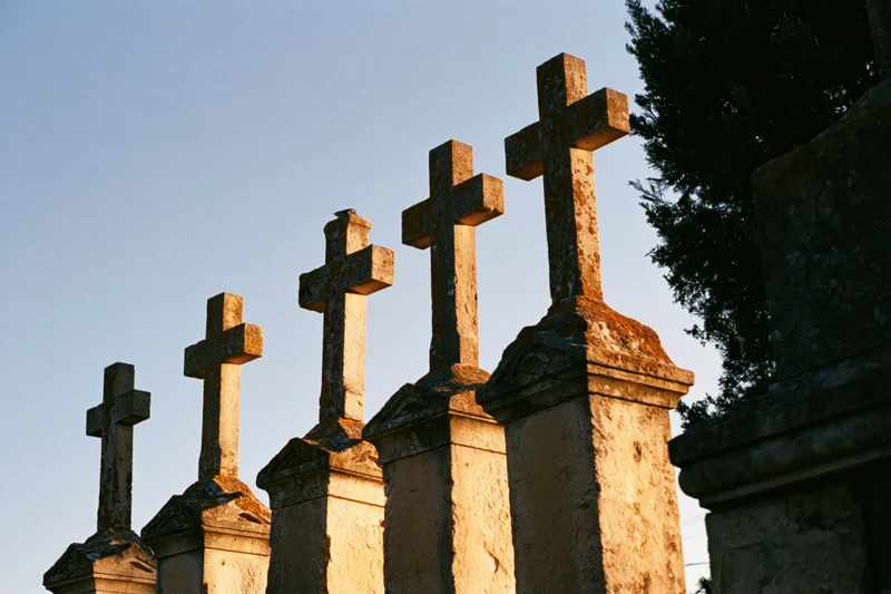 Row of weathered stone crosses on tombstones in a cemetery at dusk