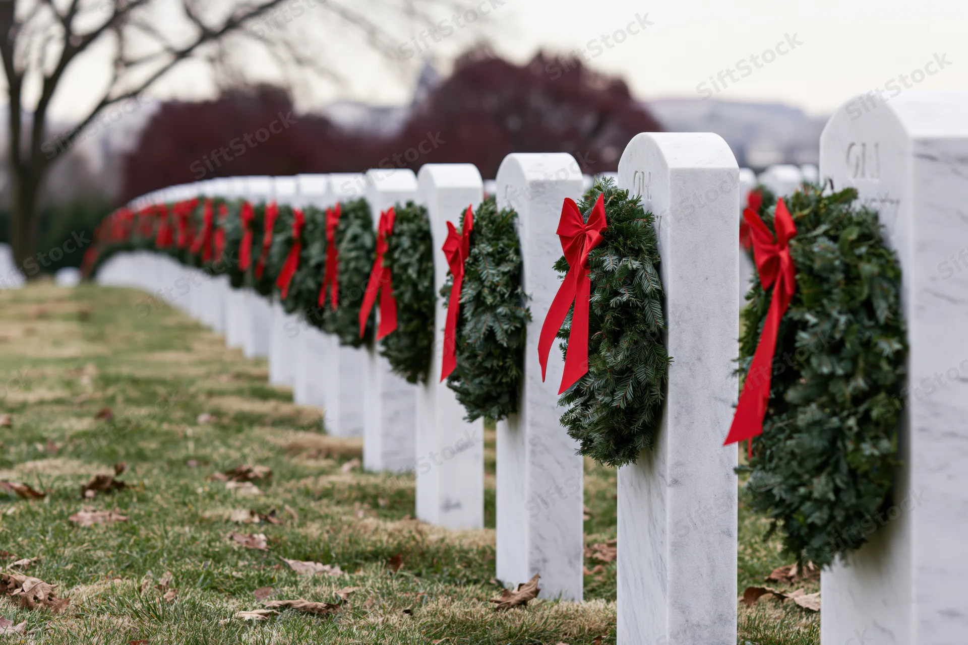 Rows of white marble headstones in a military cemetery adorned with evergreen wreaths and red ribbons during winter