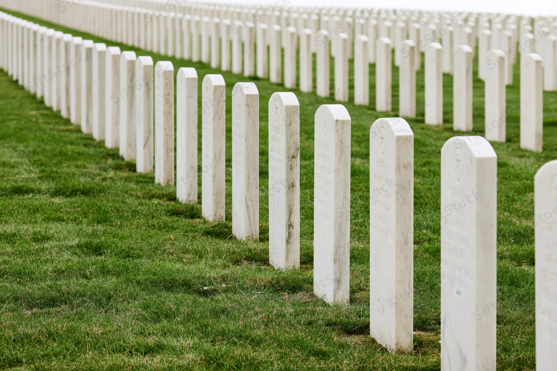 Rows of white marble military headstones aligned in neat rows across a green lawn in a national cemetery