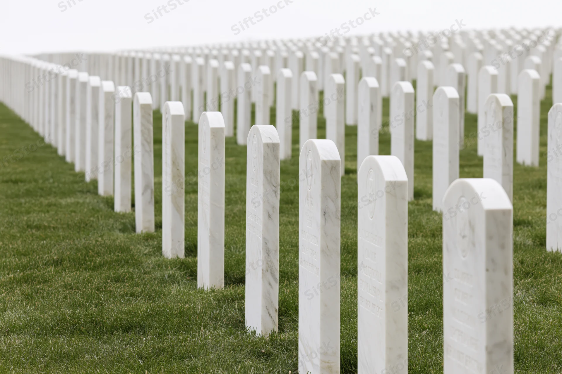 Rows of white marble military headstones aligned in neat rows across a green lawn in a national cemetery