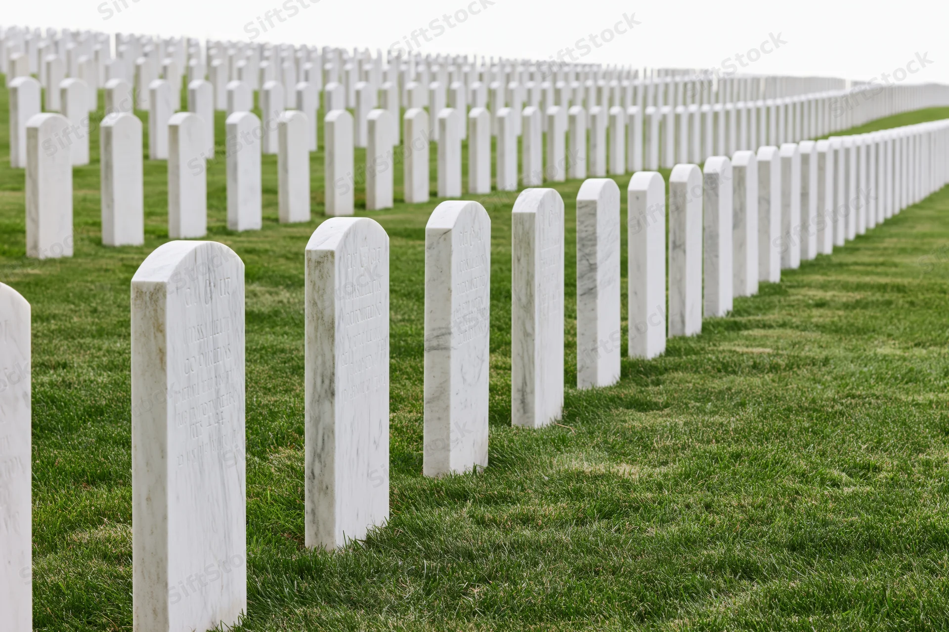 Rows of white marble military headstones aligned in neat rows across a green lawn in a national cemetery