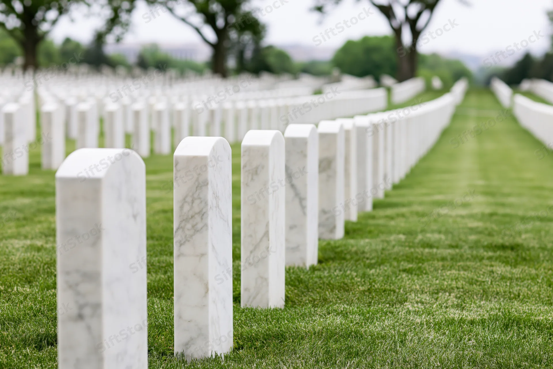 Rows of white marble military headstones aligned in neat rows across a green lawn in a cemetery