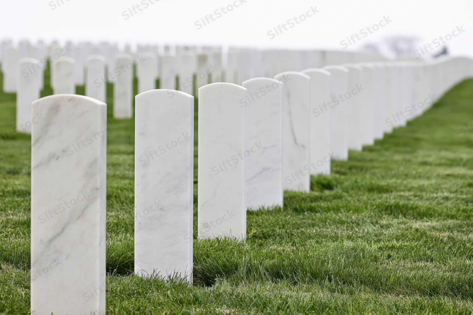 Rows of white marble military headstones aligned in neat rows across a green lawn in a cemetery
