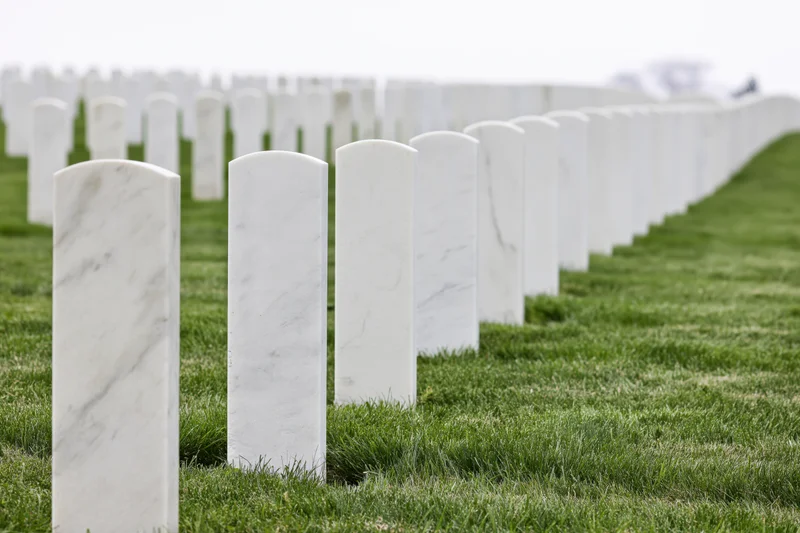 Rows of white marble military headstones aligned in neat rows across a green lawn in a cemetery