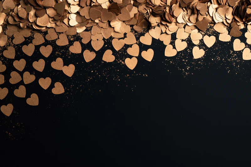 Gold metallic heart confetti scattered densely along the top of a black surface, leaving copyspace below