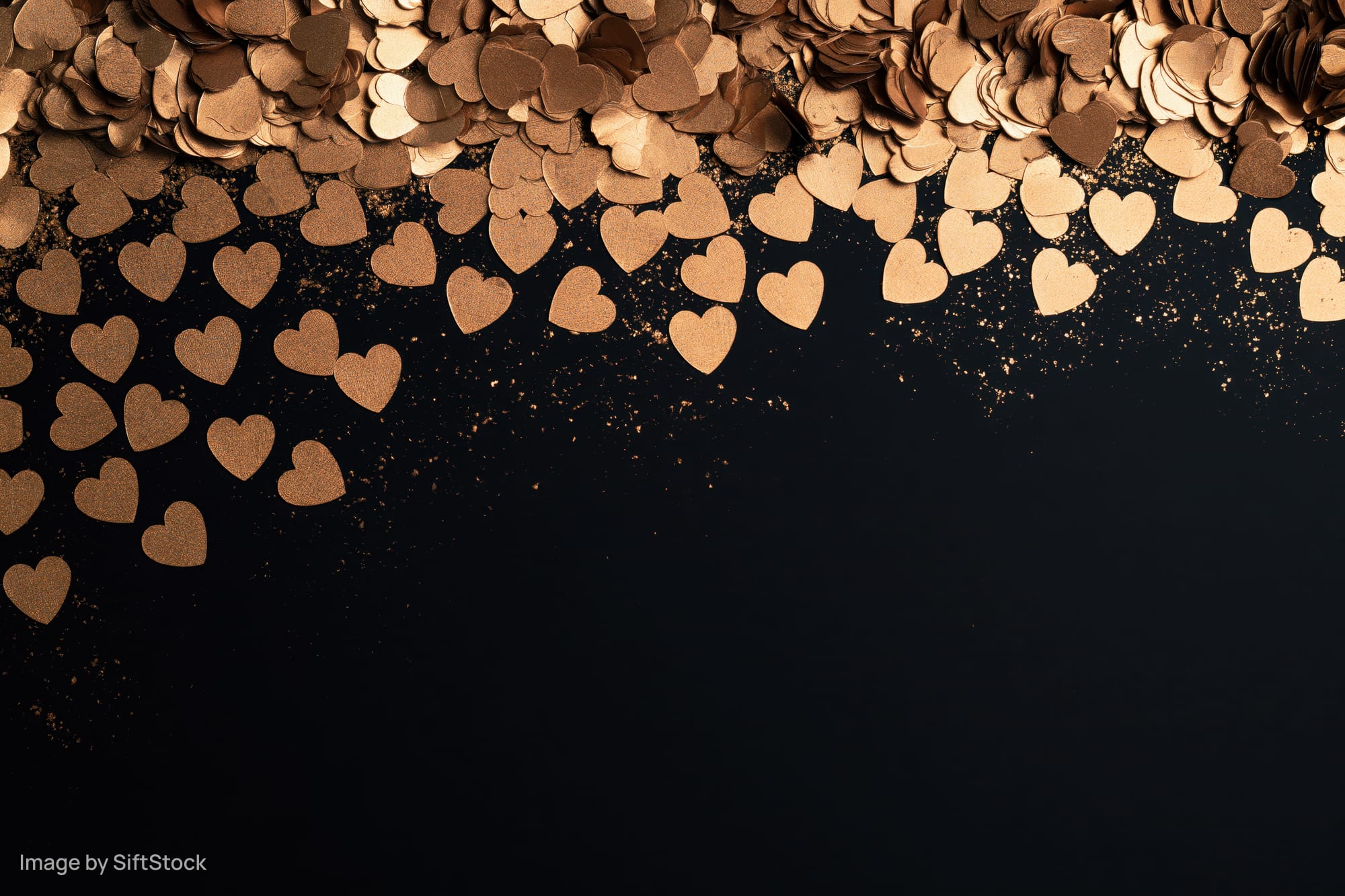 Gold metallic heart confetti scattered densely along the top of a black surface, leaving copyspace below