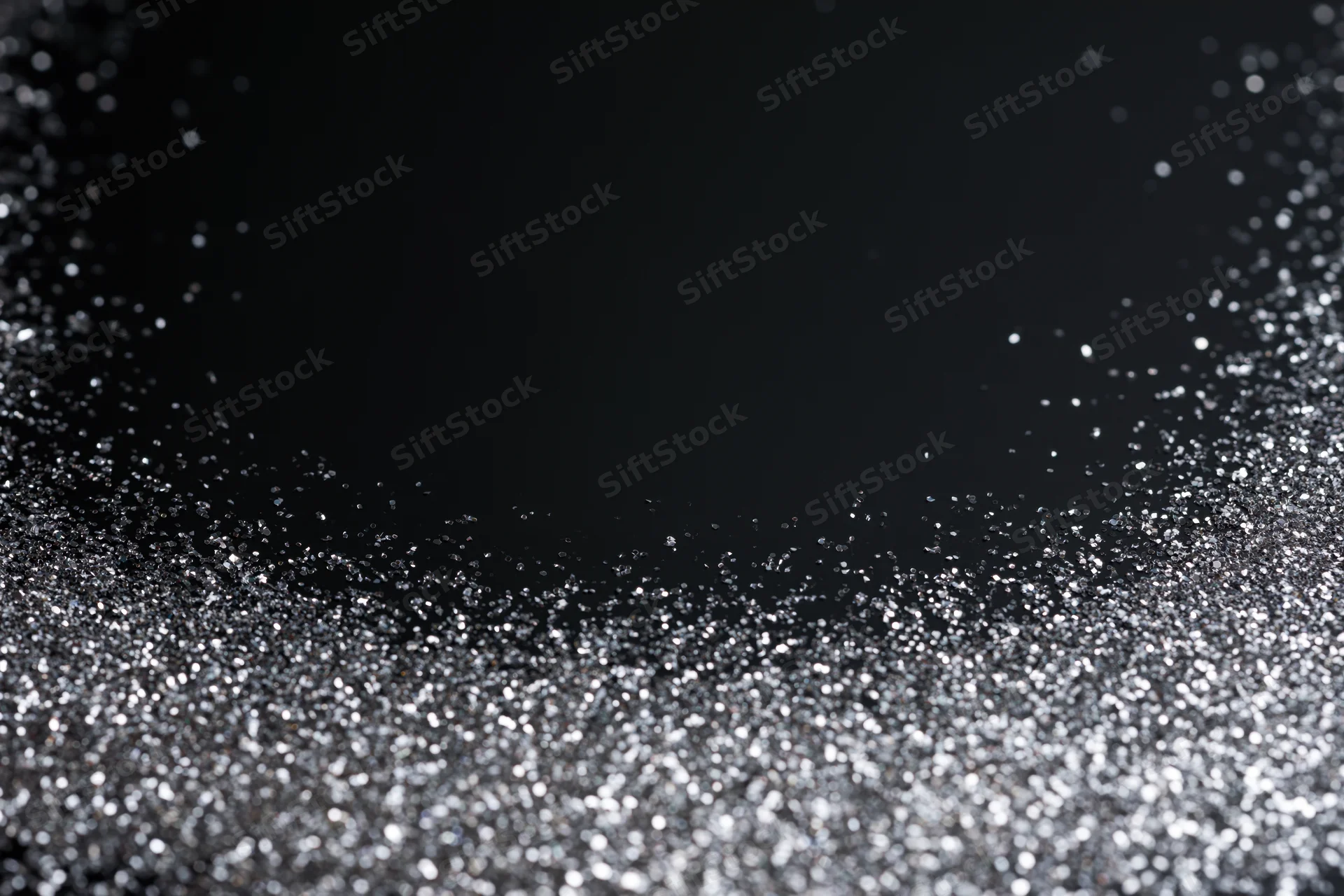 Silver glitter particles scattered across a dark surface, creating a sparkling abstract texture
