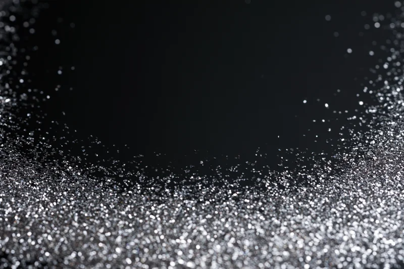 Silver glitter particles scattered across a dark surface, creating a sparkling abstract texture