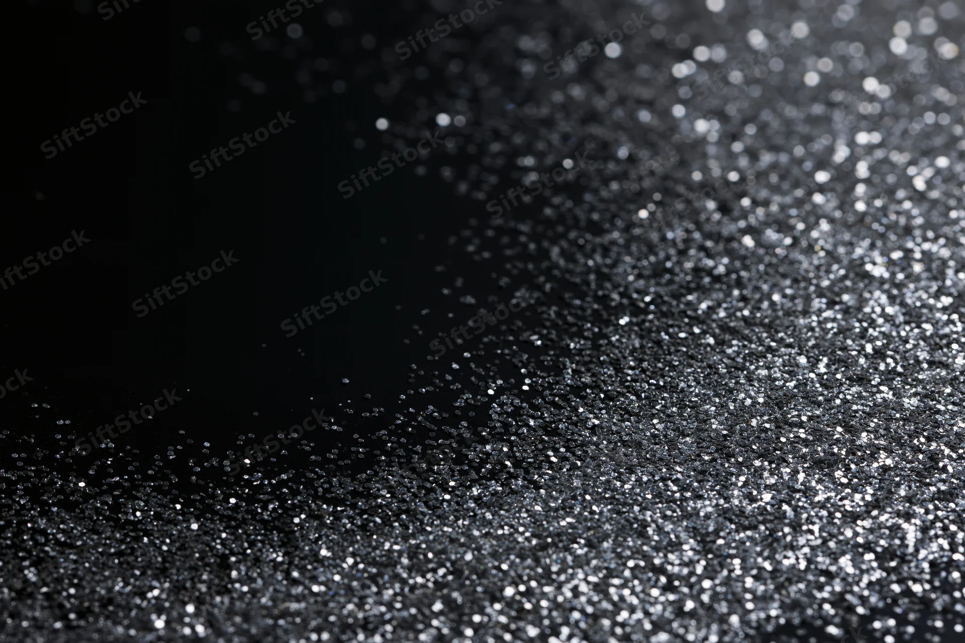 Silver glitter particles scattered across a dark surface with bokeh highlights and copyspace on the left