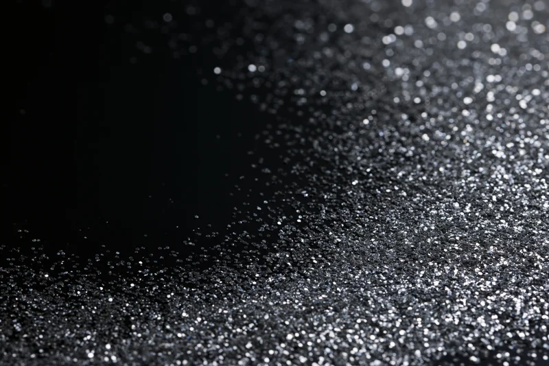 Silver glitter particles scattered across a dark surface with bokeh highlights and copyspace on the left