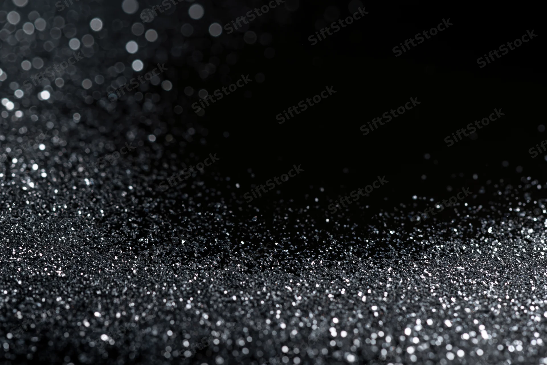 Silver glitter particles scattered and settling on a dark surface with bokeh highlights