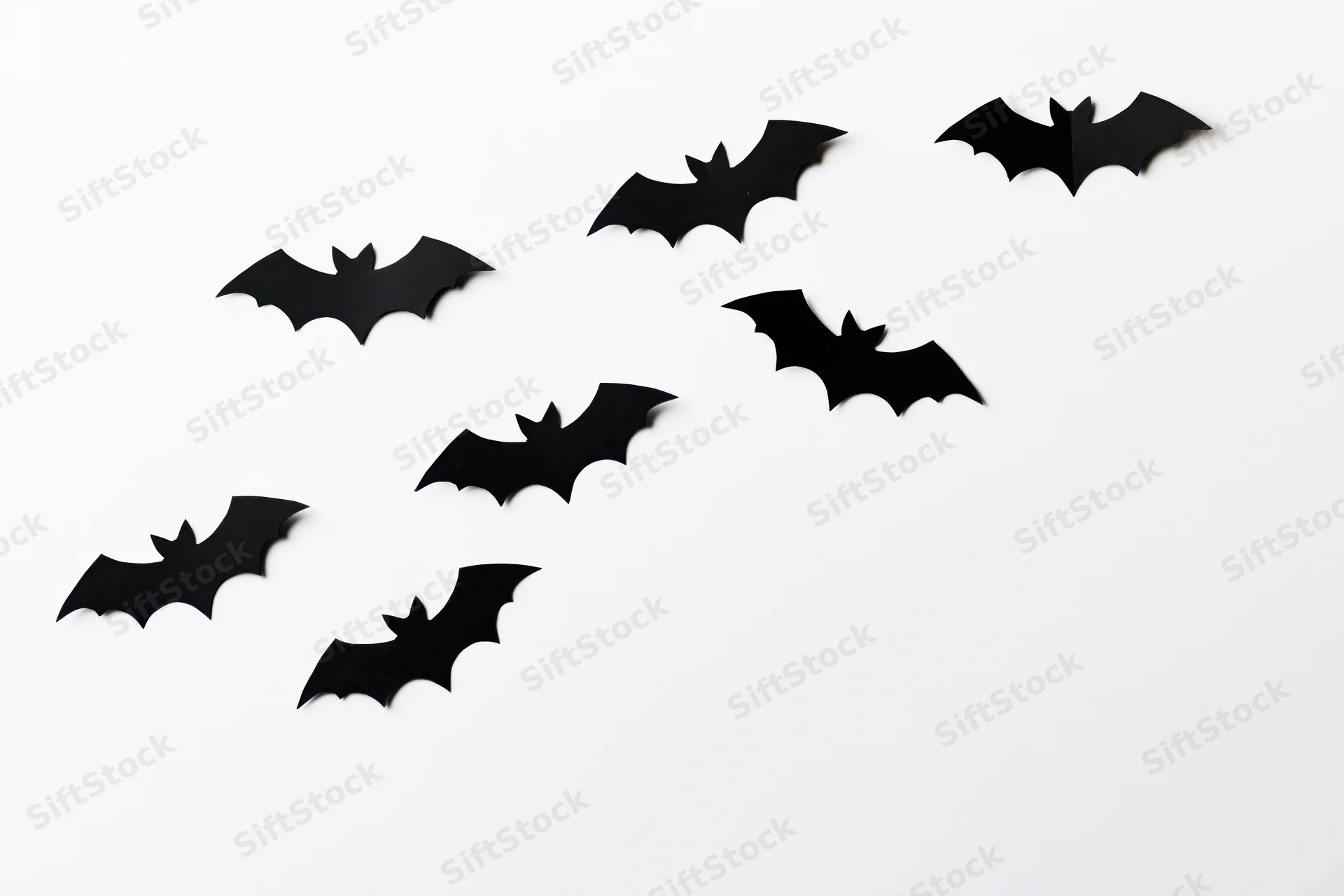 Seven black paper bat cutouts arranged diagonally on white background